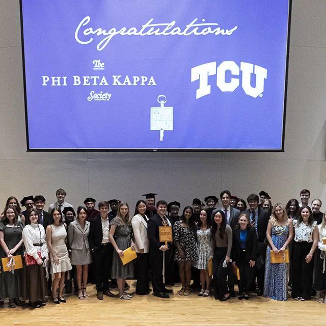 Phi Beta Kappa students gather in a large semi-circle in front of a wall projection that says 'Congratulations - The Phi Beta Kappa Society'
