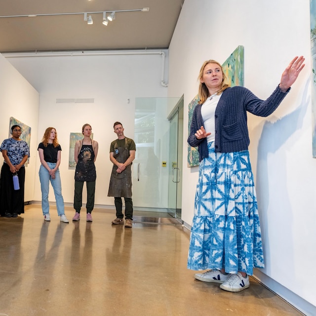 Student points to artwork in a gallery as group of people looks on