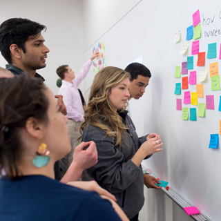 Neeley School of Business Students at a whiteboard arranging brightly colored sticky notes as part of a design thinking project