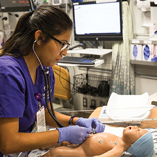 Harris College of Nursing & Health Sciences A nursing student in purple scrubs uses a stethoscope as she practices on an infant simulation dummy