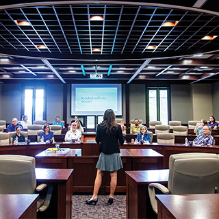 Honors College A young woman in a suit speaks before a room full of TCU Honors professors