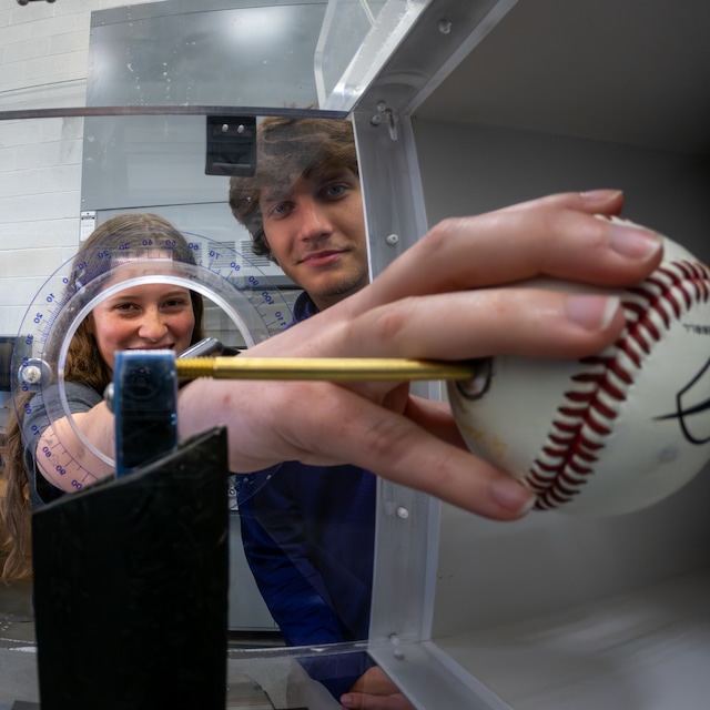 Two students test the aerodynamic properties of a baseball in a wind tunnel