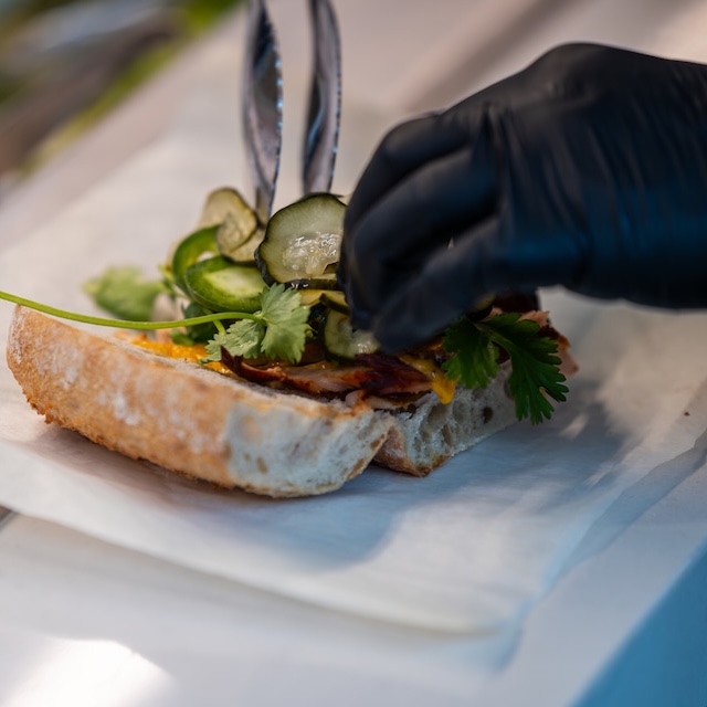 A gloved hand assembles a sandwich