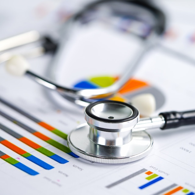 A stethoscope sits on top of papers showing graphs