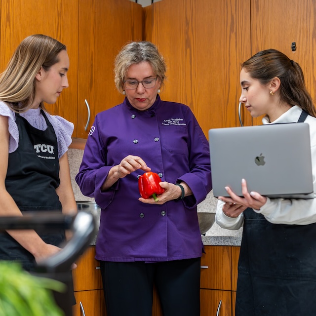 Two nutrition students look as professor points to bell pepper