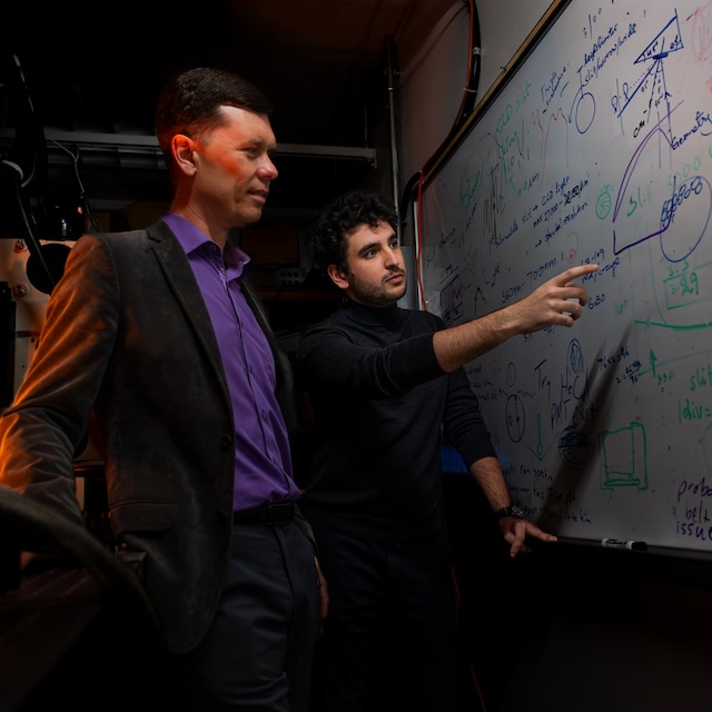 A professor and student review calculations on a dry erase board