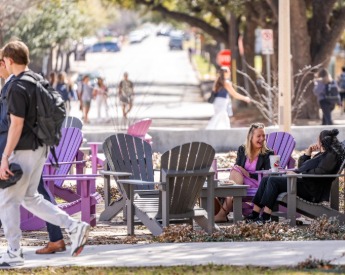 Students laughing during a conversation while seated in purple adirondack chairs.